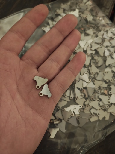 Holding two small metal pieces with many more in the background